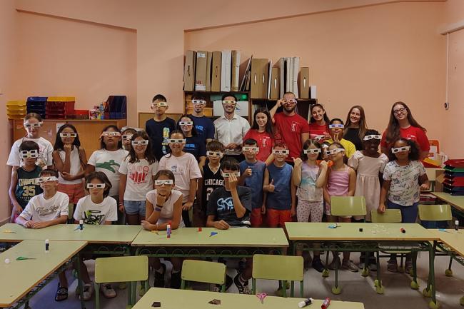 El alcalde, Alejandro Navarro, y el joven estudiante, Alejandro Mena, con los niños que participan en las Colevacaciones posando con las gafas que han realizado para disfrutar del eclipse con todas las garantías 